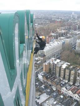 Choosing Special Abseiling Services can save time and money. Man working on a Holiday Inn sign, abseiling from a rope.